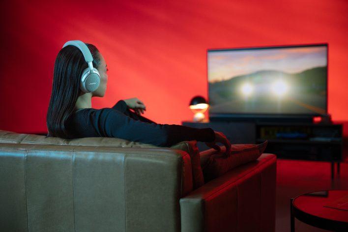 A woman using SimpleSync wearing Bose QuietComfort Ultra Headphones to watch TV with a Bose Smart Ultra Soundbar